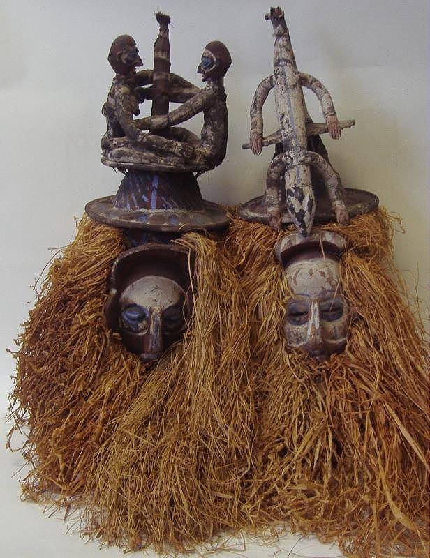 2 African Carved Wood & Painted Headdress Masks: Two African carved wood headdress masks. With polychrome painted faces. Grasses used for the hair and beards. Painted cloth headdress at the top of the masks. Wood holding handle on the interior. Each