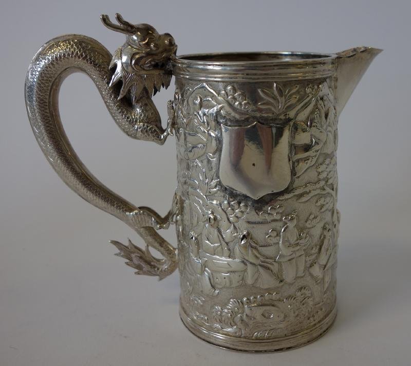 Chinese Export Silver Pitcher, Dragon Handle, Sgnd: Chinese Export silver cream pitcher. 19th century. Well defined dragon formed handle. Overall embossed motif depicting mandarin figures in a landscape village setting. Signed underfoot. Measures 4.75"