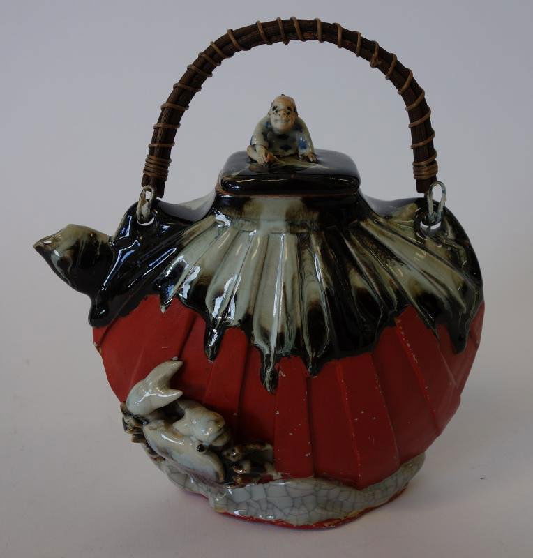 Japanese Sumida Gawa Earthenware Teapot: Japanese Sumidagawa earthenware teapot. The finial depicts a seated male figure. Raised crab and sea motif. Measures 6.75" high to top of finial, 7" long and 3.5" wide.