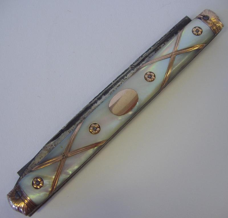 Mother of Pearl & Gold Double Pocket Knife: Mother of pearl pocket knife. Each side inset with a gold medallion, strap banding and rosettes. Two fold-out knives. Measures 4.5" long closed. 12" long when opened.