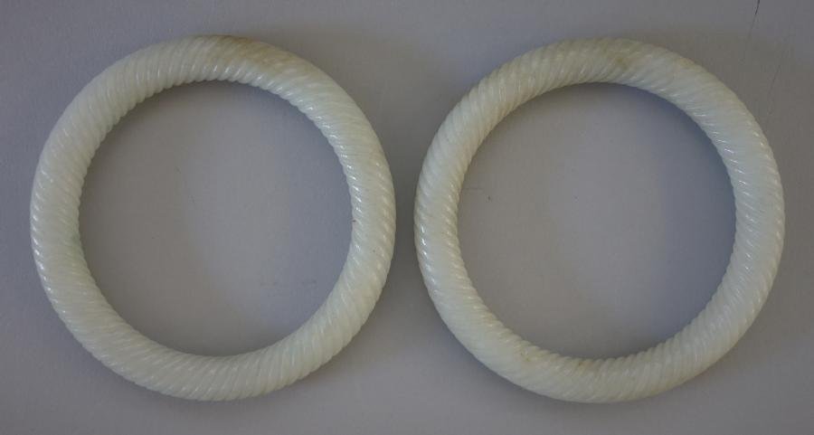 Chinese Carved White Jade Bangle Bracelets, Pair: Well carved pair of white jade bangle bracelets. Early 20th century. Each measuring 3-1/8" in diameter. Inside circumference 7.5". NOTE: faint hairline to each.