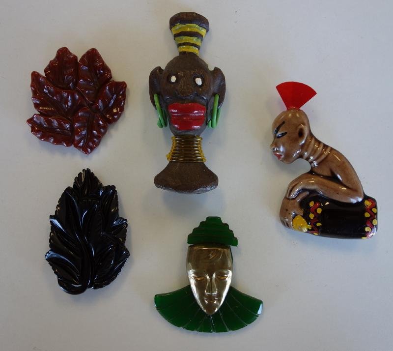 Bakelite Brooch Clips & Painted African Jewelry: Five brooch clip / pins. Comprised of three bakelite brooches measuring approximately 2.25" high. Together with a painted plaster figure of an African woman with an amber headdress and a painted Afric