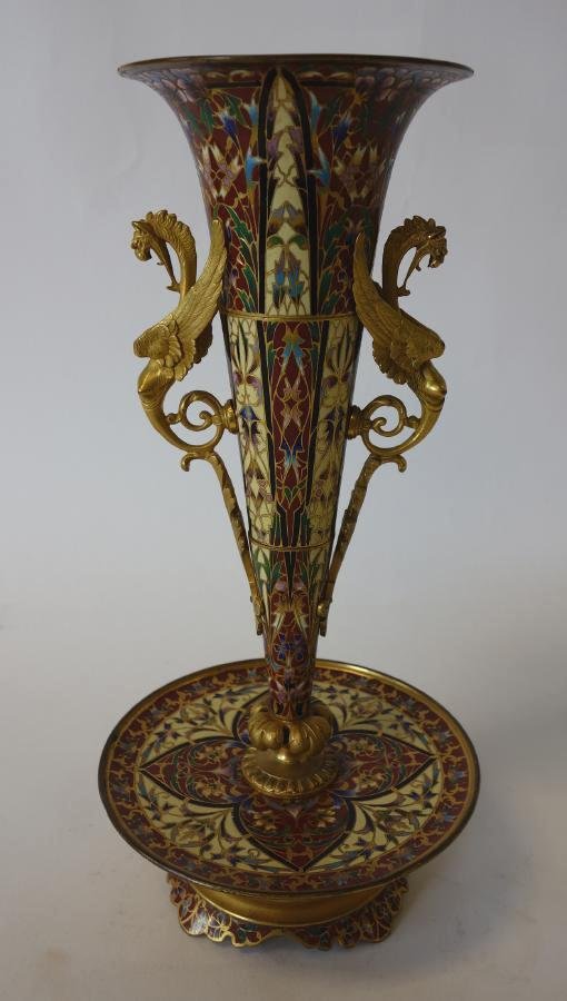 French Enamel & Gilt Bonze Vase, Griffin Handles: A French champleve enameled and gilt bronze centerpiece vase. Tapering cylindrical form with tazza base. Overall floral motif. Stylized griffin formed handles. Measures 13.25" high and 6.25" in diamet