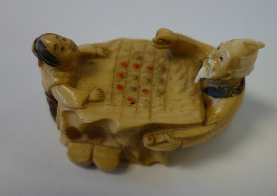 Carved Ivory Netsuke Figural Game Scene: A Japanese carved ivory netsuke. Figural grouping depicting an elder male playing the board game of Go with a child. Signed on the underside. Measures 2.25" long, 1-3/8" wide and 1-3/8" high. NOTE: It
