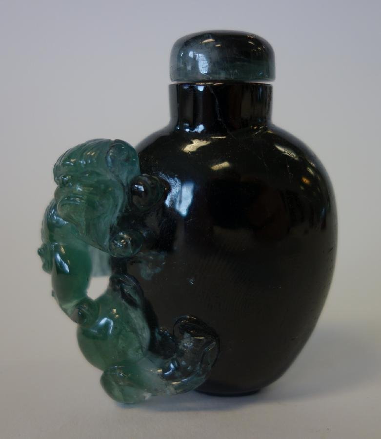 Chinese Green Agate Snuff Bottle: A Chinese hollowed-out deep green agate snuff bottle, with a lighter green carving depicting a foo dog / lion on a ball. Measures 2.5" high x 2" high.