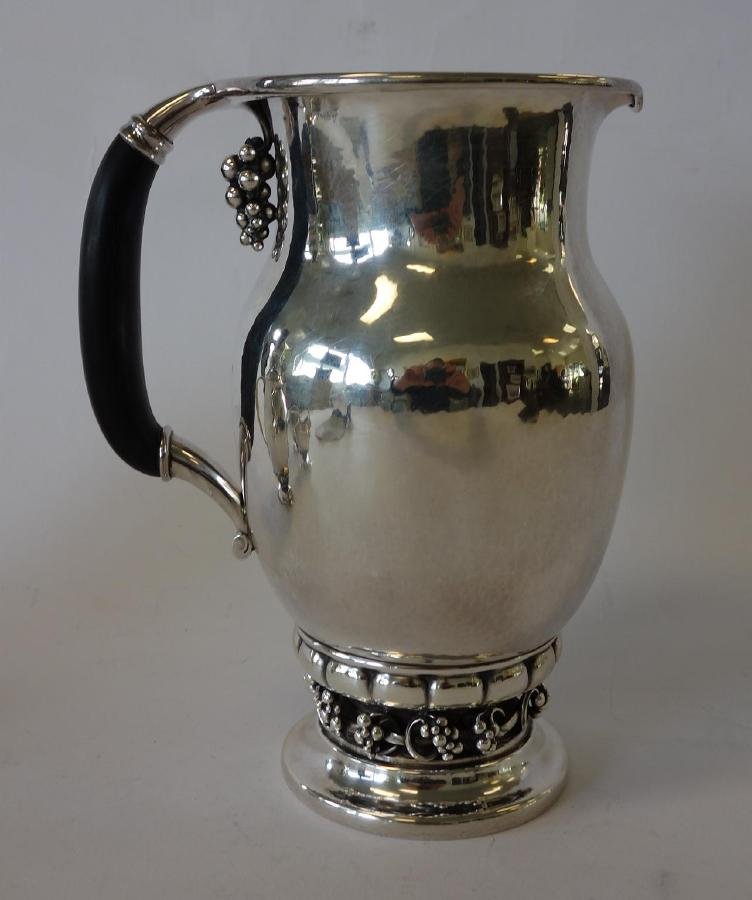 Georg Jensen Sterling Water Pitcher, Pattern 407A: A sterling silver water pitcher by Georg Jensen. Grape pattern 407A, c.1945-77. Baluster form. The base and the underside of the handle with applied scrolling grapes. Ebonized wood handle. Signed unde