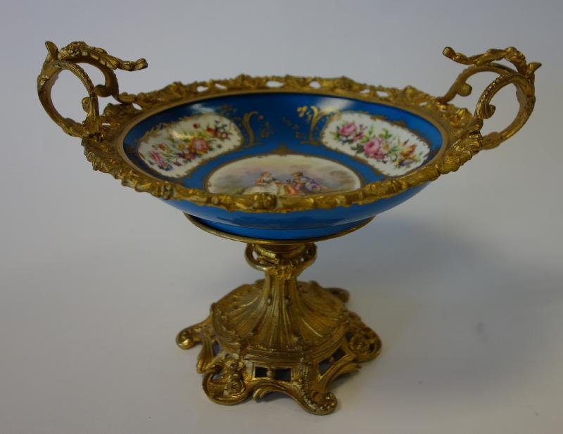 Sevres Style Porcelain & Gilt Metal Compote: A Sevres-style porcelain and gilt metal compote. Hand-painted decoration depicting a courting couple within a landscape setting, surrounded by panels of flowers. Signed on the underside of the porcela