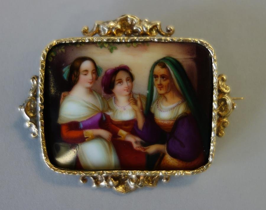 Painted Porcelain Plaque in 14K Gold Brooch: A painting on porcelain set in a 14K gold frame and backed with a pin. The well detailed portrait depicts a mother offering guidance to her two daughters. The plaque measures 1.25" x 1-5/8". The frame