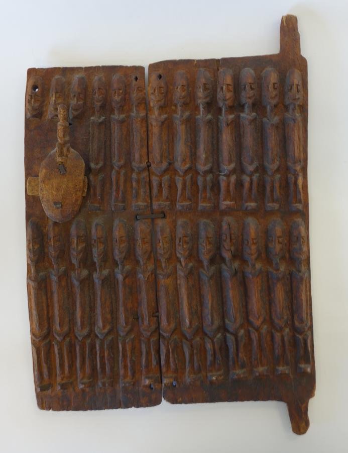 African Dogon Tribe Granary Door: An African carved wood granary door. Dogon tribe. Carved to depict male elongated abstract figures. Figural lock / latch. Measures 18.75" high x 15" wide, 23" high to top and bottom flange.