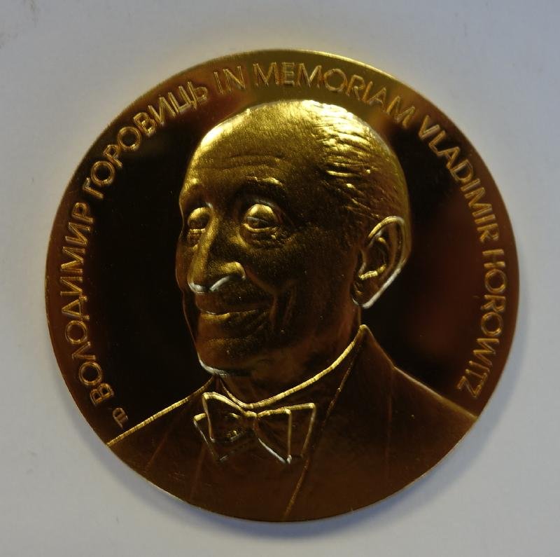 Vladimir Horowitz Commemorative Gold Medal: Vladimir Horowitz commemorative gold medal. From the 1999 International Competition of Young Pianists. The medal / coin measures 44mm. The obverse has a bust of Horowitz. The reverse showing hands on 