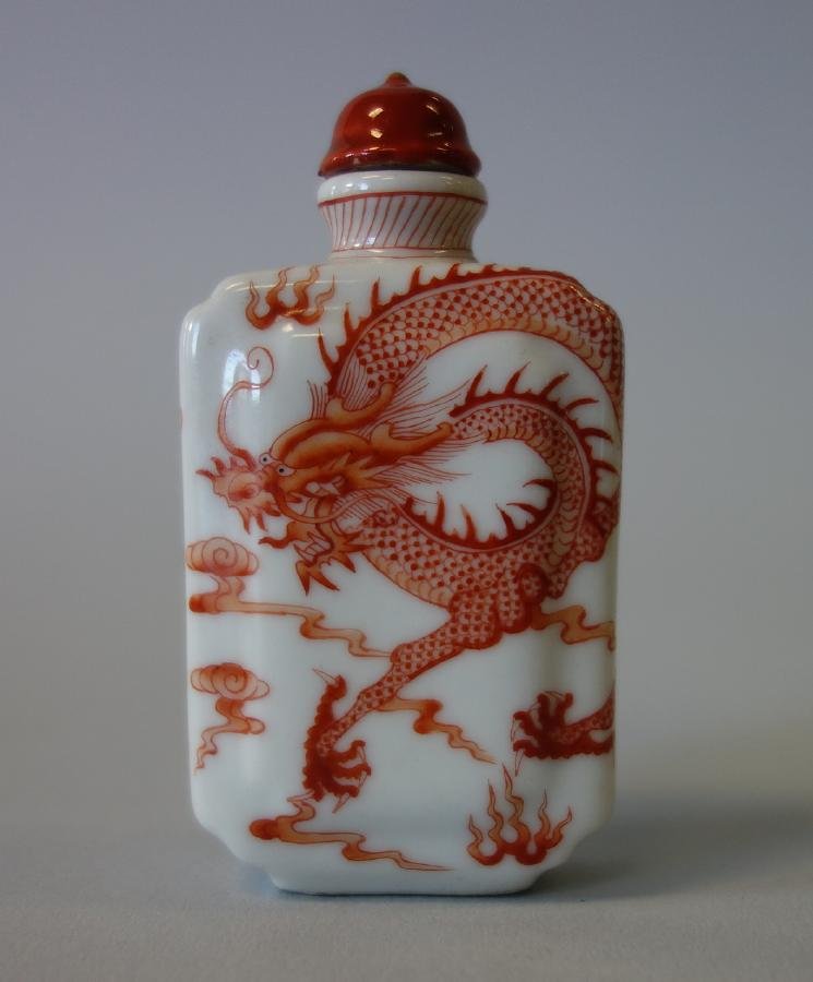 Chinese Iron Red Porcelain Snuff Bottle, Qing Mark: A Chinese porcelain snuff bottle. Iron red enamels depicting a five claw dragon among clouds, chasing the pearl of wisdom. Signed underfoot with a 3-character Qing Dynasty mark. Measures 2-5/8" high.
