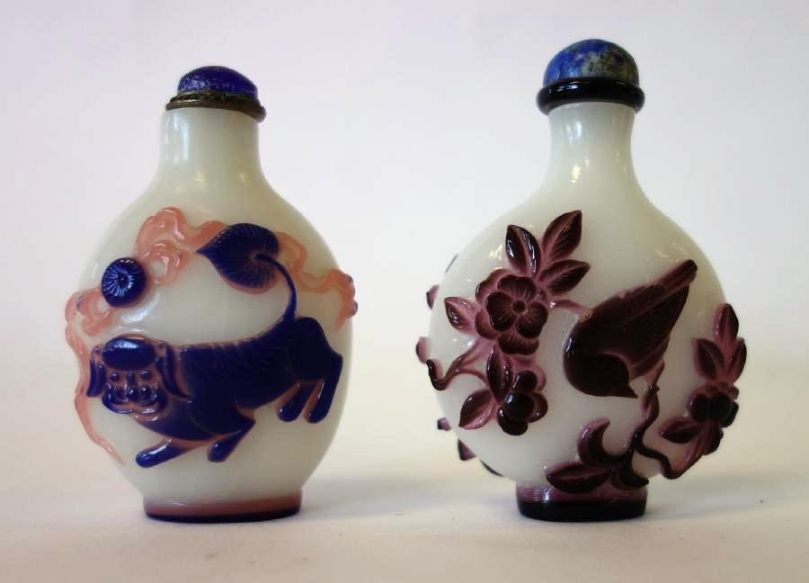 2 Chinese Peking Cameo Glass Snuff Bottles: 2 Chinese Peking cameo glass snuff bottles. A white milk glass bottle with cameo overlay depicting playful foo dogs / lions. Together with a bottle decorated with amethyst glass depicting birds in a f