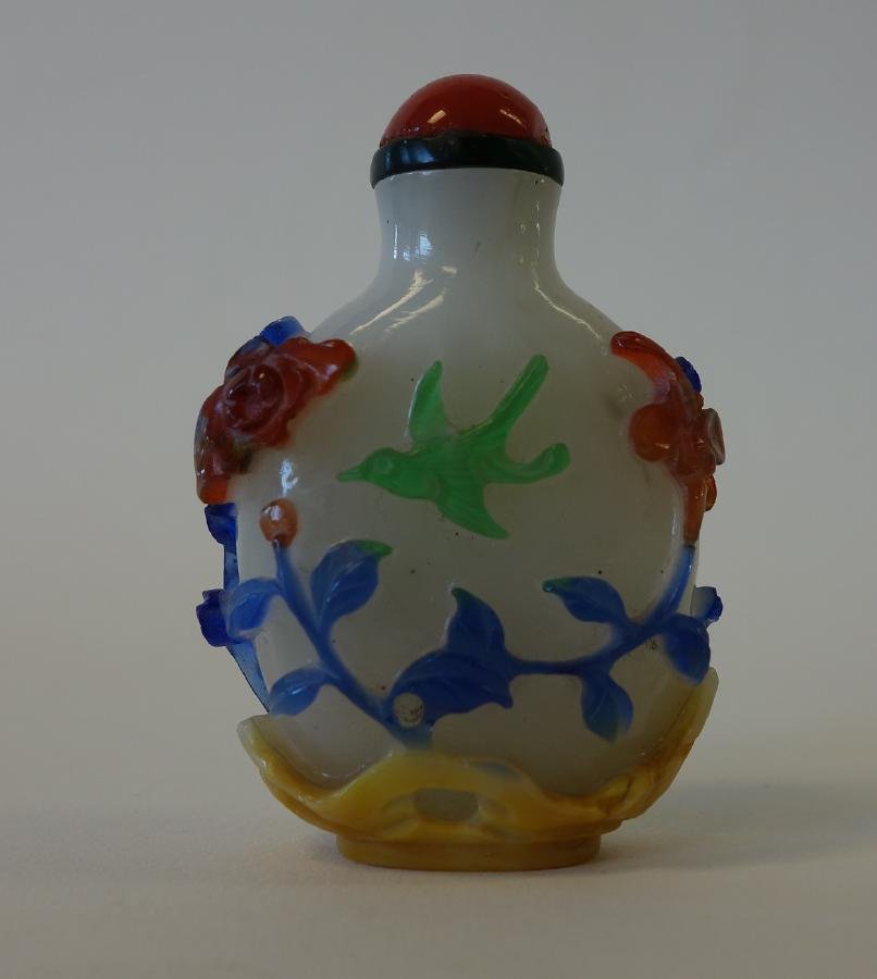 4-Color Overlay Cameo Glass Snuff Bottle: A Chinese overlay cameo glass snuff bottle. 19th century. White bottle decorated with a four color glass overlay depicting birds within a floral setting. Measures 2-3/8" high to top of stone cap.