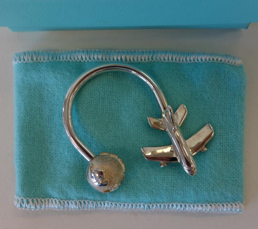 Tiffany & Co Sterling Airplane Key Chain Ring: A Tiffany & Co. sterling silver key ring / key chain. Formed as an airplane going around the world. Measures 1.75" x 1.5". Comes with the original velvet pouch and box.