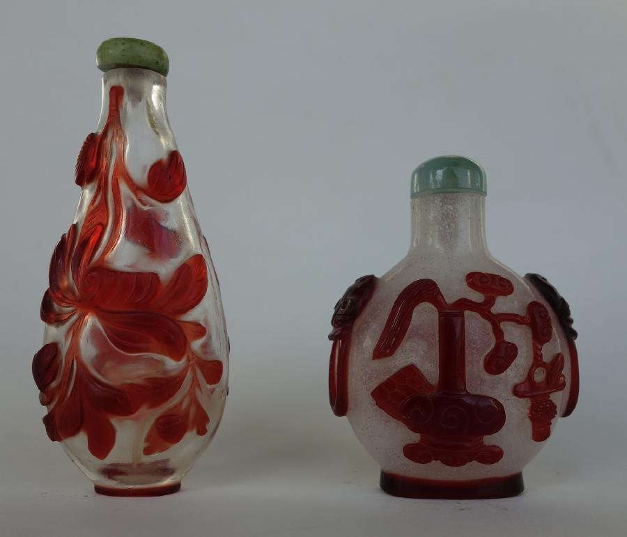 2 Chinese Overlay Cameo Glass Snuff Bottles: Two Chinese overlay cameo glass snuff bottles. One bottle of opaque glass with ruby red overlay depicting urns of flowers and mask-formed side handles, 2-3/8" high to top of jadeite cap. Together with