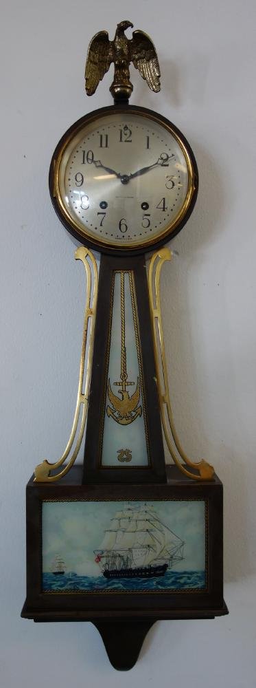 Seth Thomas Banjo Clock, Nautical Theme: A Seth Thomas banjo clock. Mahogany case, surmounted by a brass eagle. Brass side ornaments flank the waist section decorated with an American eagle perched on a roped anchor above a pair of seahorses