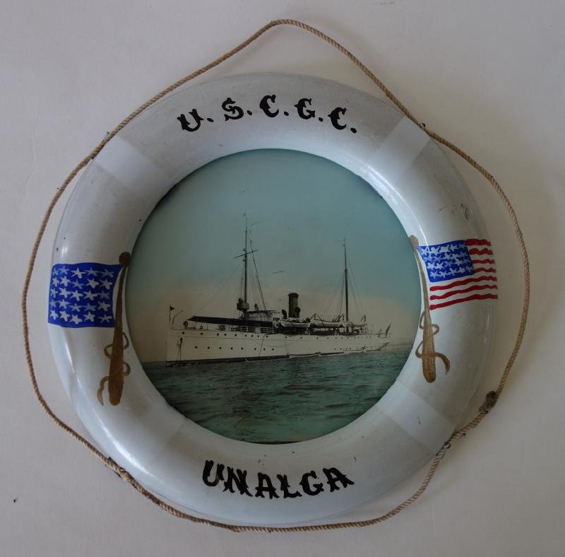 Cutter Unalga Photo & Life Preserver Frame: A vintage colored photo of the U.S.C.G.C. Coast Guard Cutter Unalga, c.1912. Housed in a porcelain nautical themed life preserver frame. Measures 9" in diameter. The opening measures 5.75" in diameter
