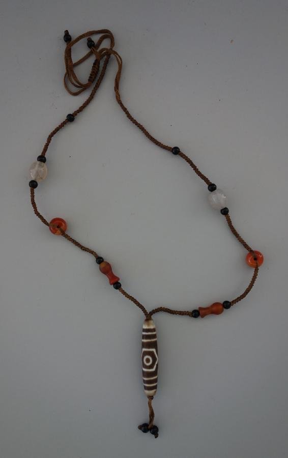 Tibetan Dzi Stone & Carnelian Bead Necklace: A Tibetan necklace set with a large oblong Dzi bead attached to a woven cord with varying sized and shaped carnelian stones. The dzi bead measures 2.25" long. The Dzi stone is said to have positive sp