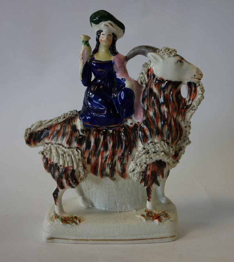 19thc Staffordshire Girl on Bearded Camel: An English Staffordshire porcelain figure, 19th century. Depicts a young girl riding on a bearded camel, with a parrot at her shoulder. Measures 10" high, 8" wide, 2.75" deep. NOTE: Hairlines and craz