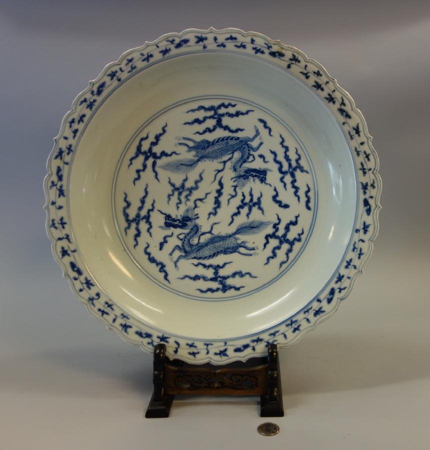 Chinese Porcelain Charger Bowl, Signed: A Chinese blue and white porcelain charger / shallow centerpiece bowl. Scalloped edged bowl with underglaze blue enamels depicting two mythological flying dragons among stylized clouds. Floral border.