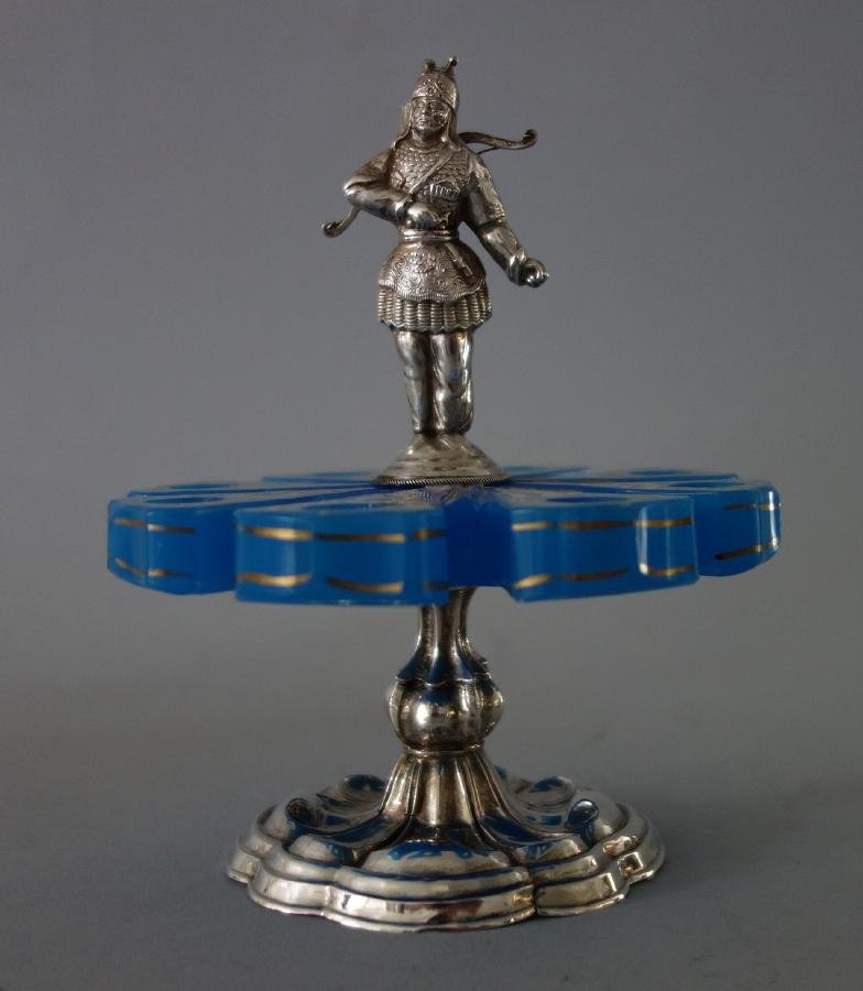 French Opaline Glass & Silver Flower Frog: A French blue opaline glass and silver flower frog. Enamel painted flower-formed glass holder with attached male archer, the quiver formed to hold a small bud. Scalloped edged silver base, indistinctl