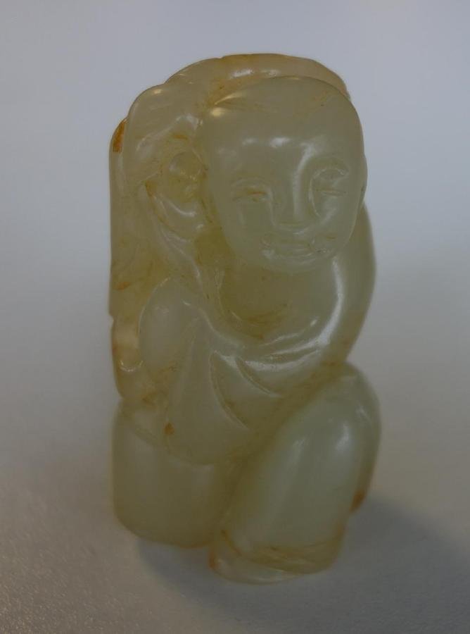 Chinese White Jade & Russet Toggle, Young Boy: A Chinese white jade toggle. Finely carved translucent white jade with russet inclusions, depicting a young boy holding a lotus branch with foliage. Measures 1.75" high, 1" wide, .75" deep.