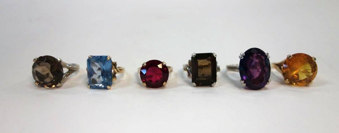 6 Semi Precious & 10K Gold Cocktail Rings: A group of six cocktail rings. Semi-precious solitaire rings each set in 10K gold. Amethyst, Topaz, Citrine, Ruby, Smokey Quartz & Tourmaline. Ring sizes 5 to approximately 5.75. Overall weight includ