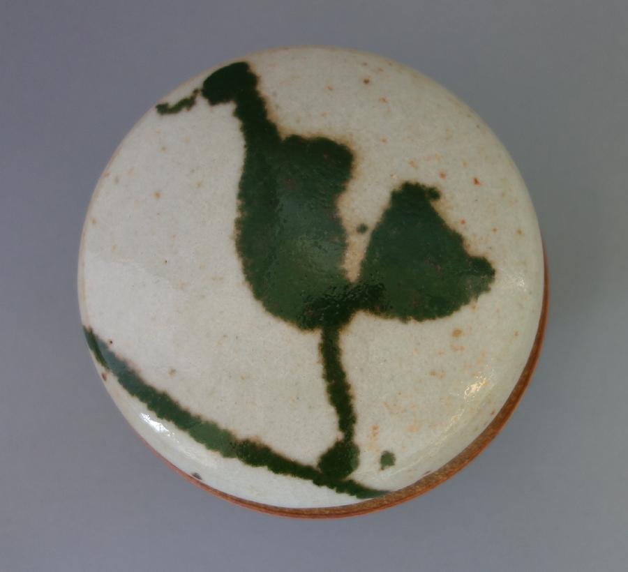 Warren Mackenzie, Glazed Stoneware Box: A glazed stoneware lidded box by Warren MacKenzie (b-1924). Stylized green decoration on lid. Faint artist's cipher at foot of rim. Measures 5.25" diameter, 3.75" high. MacKenzie is the first American