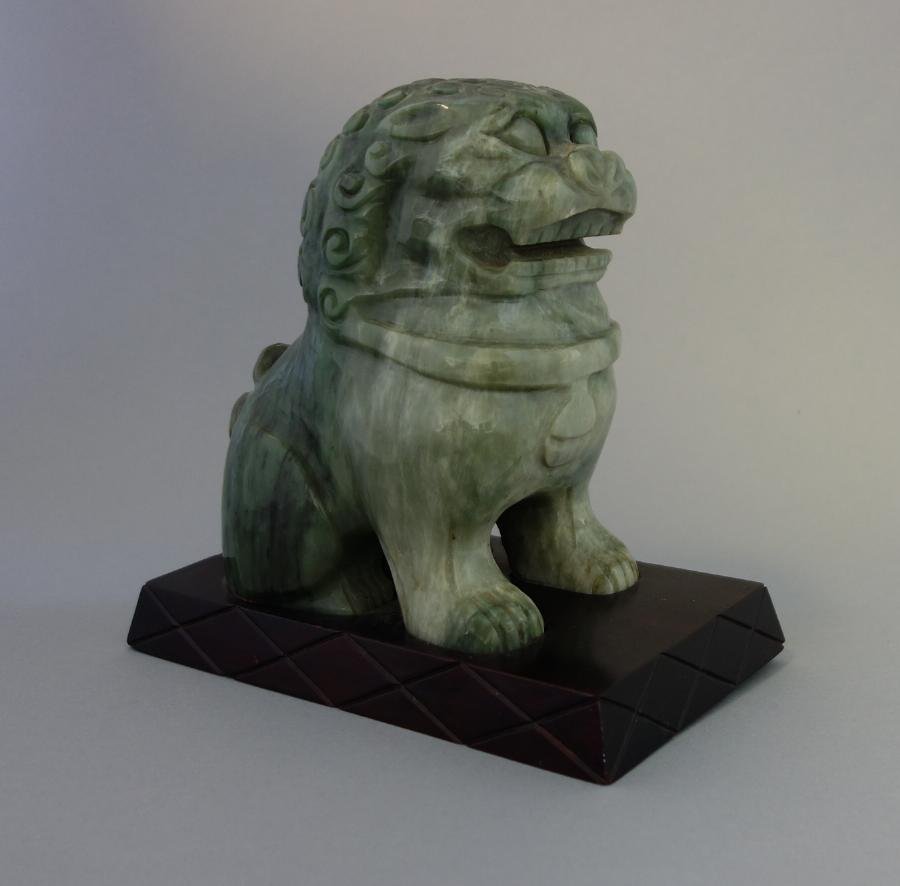 Chinese Jade Foo Dog / Temple Lion: A Chinese jade model of a foo dog or temple lion. Well carved and mounted in a fitted wood stand. Overall height in stand, 7". The base of the stand measures 7-1/8" x 4-1/8".