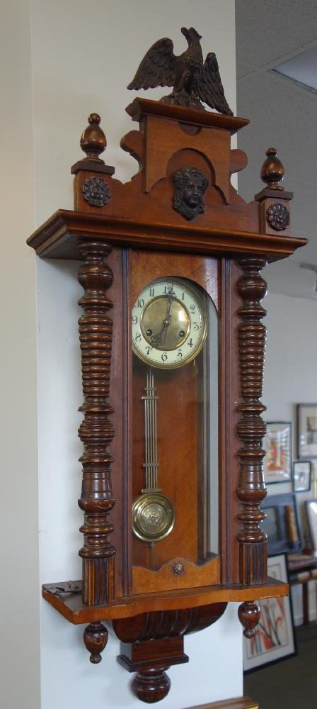 19thc DRCM German Walnut Wall Clock: German wall clock. Late 19th century. Marked "DRCM" on works. The walnut case surmounted by an eagle with carved rosettes flanking a female face. Pendulum with embossed figure of a winged fairy with f