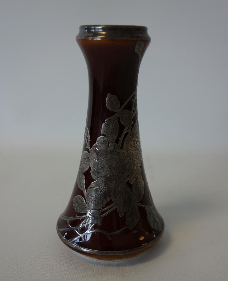 English Art Pottery Vase, Sterling Silver Overlay: An English Art Pottery vase. Sterling silver overlay over a brown glaze depicting flowers, vines and leaves. Measures 5.75" high, 3" diameter at the base. Signed underfoot with a Unicorn and England.