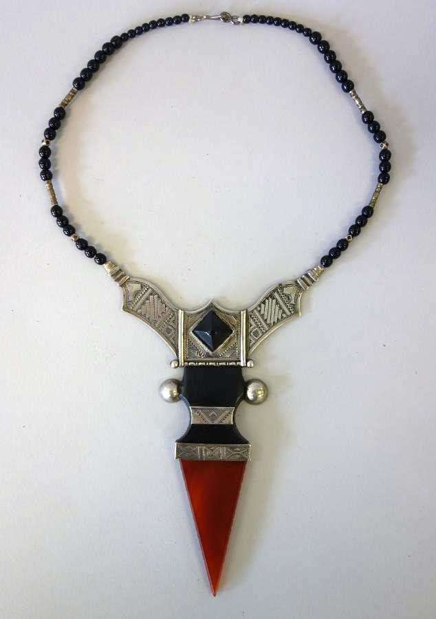 Tuareg Sahara Pendant Necklace: A Tuareg Sahara pendant necklace. The pendant composed of etched and chased silver with carnelian and ebonized wood. Attached to a black onyx beaded necklace. Maker's cipher on the reverse. The pendan