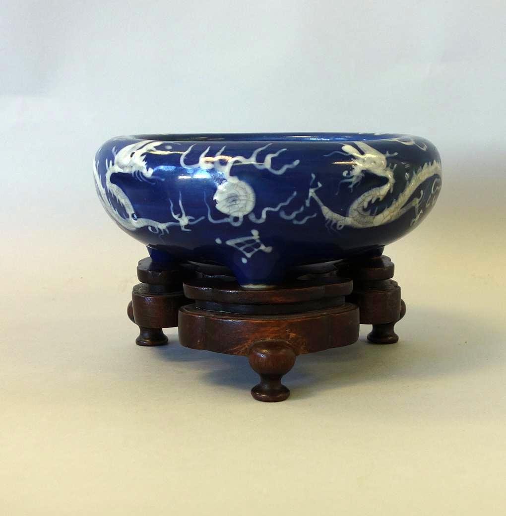 Asian Cobalt Blue Porcelain Censer, Dragon Motif: An Asian porcelain tri-footed censer. Cobalt blue ground decorated in white slip depicting dragons among stylized clouds, pursuing the flaming pearl of wisdom. Inverted rim. Measures 8.75" diameter, 3