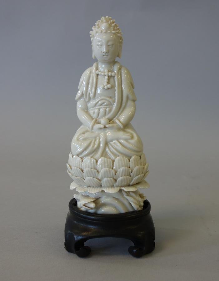 Chinese Blanc de Chine Porcelain Figure of Buddha: A Chinese Blanc de Chine porcelain figure of Buddha. The figure in a lotus position rests upon a lotus formed base. Measures 5-1/8" high, 2" diameter at the base. The figure sits in a fitted rosewood 