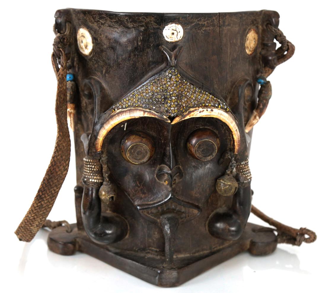 African or Oceanic Carved Ebony Shield: African ebony shield depicting the face of a god mounted with teeth and bells. [14 1/2" H x 13 1/2" W x 7 1/4" D]. Pieces detached, but present. Some losses.