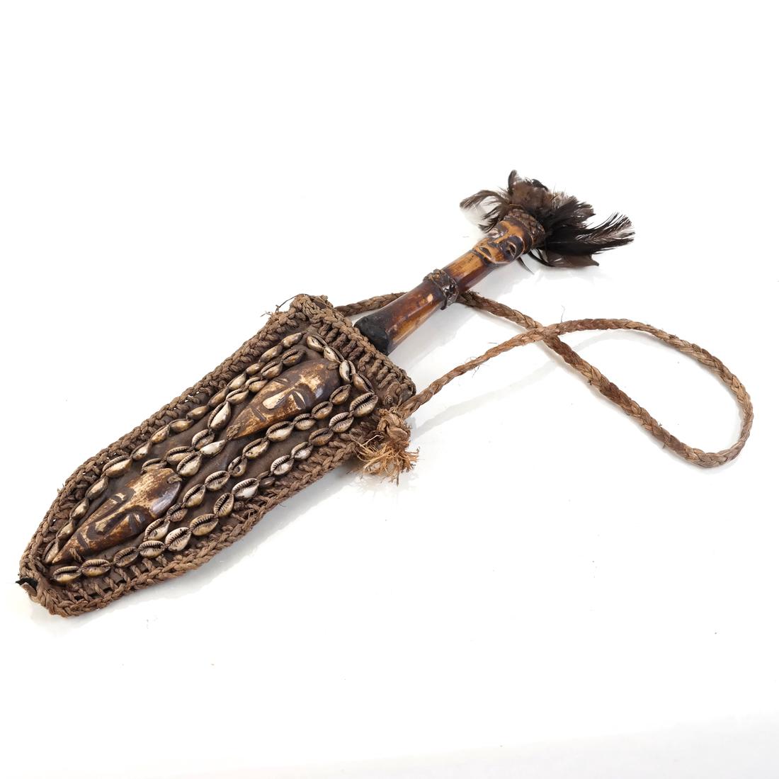 African Ceremonial Dagger: With an effigy carved bone handle in the form of a figure with feather headdress, hand forged metal blade and leather sheath decorated with bone and cowrie shells, the scabbard with two central masks.