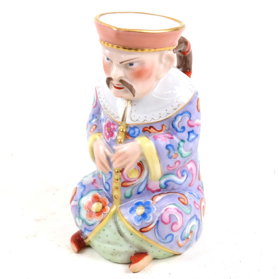 Royal KPM Small Figural Vessel: Modeled as a seated Chinese man, with his pony tail serving as the handle. [5" H x 4" W x 2 3/4" D].