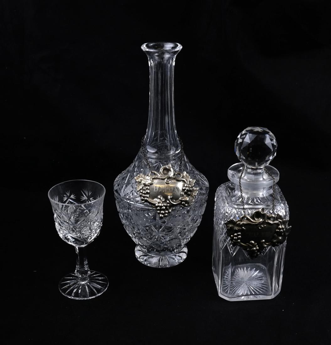 Two Cut Crystal Decanters, One Wine Glass: Comprises: 1.) Rectangular decanter with spherical stopper and silver plate bottle ticket. Engraved "cheap wine". 2.) Tall neck urn form decanter (missing stopper) with silver plate ticket engraved "B