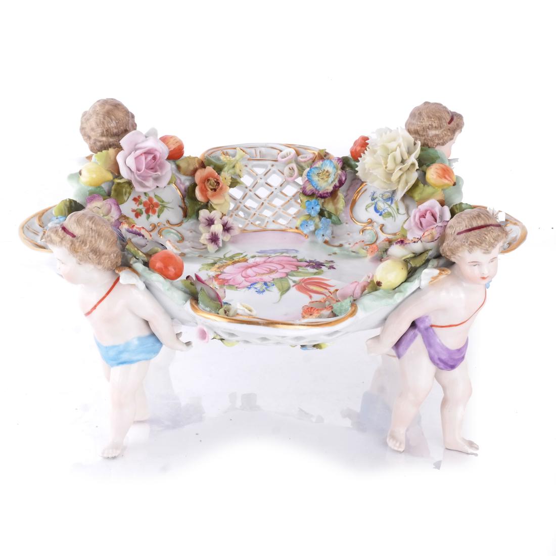 Porcelain Cherub & Floral Centerpiece: Porcelain cherub and floral decorated centerpiece. [5 1/2 x 12 (dia) inches]. One or two shallow chips to petals and one angel wing tip with shallow chip.