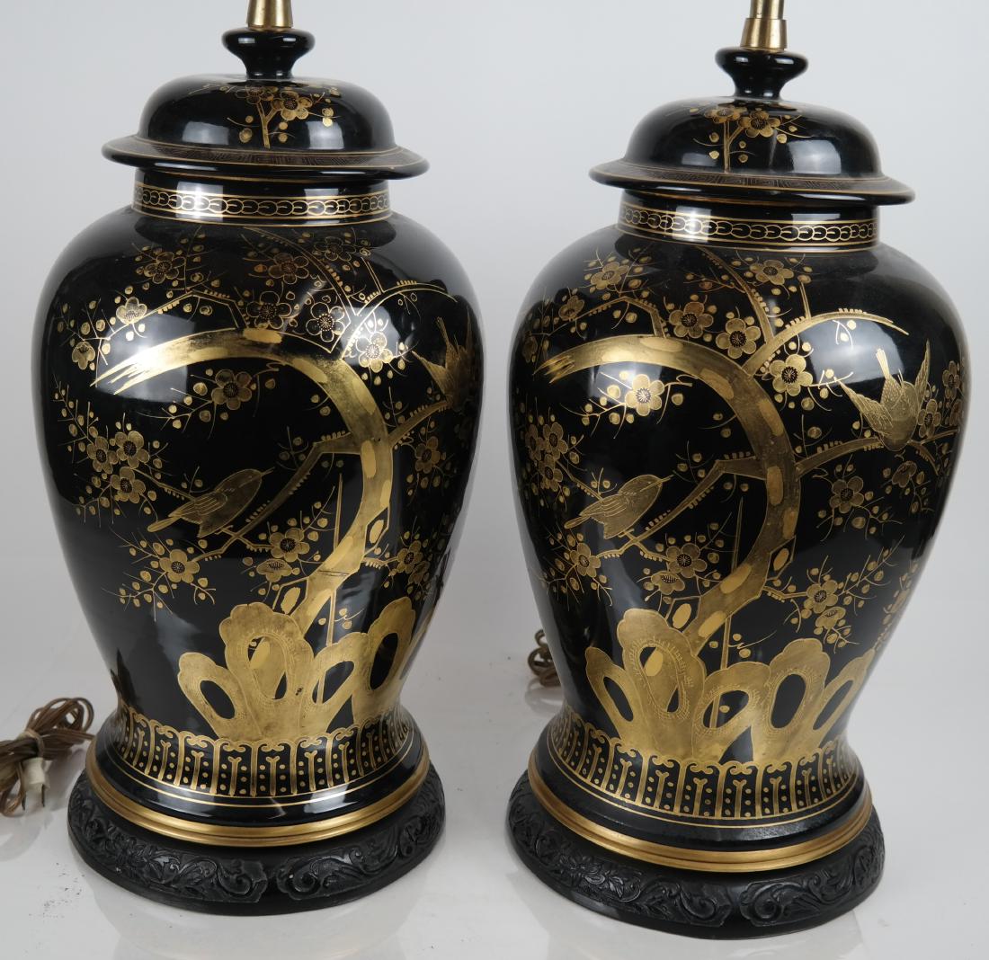 Pair Chinese Porcelain Lamps: Black ground jars converted to lamps painted with gold chrysanthemums, birds and rock motifs. On ebonized carved wood bases. [21 inches to top of jars; 27 inches H to knop; 12 (dia) inches]. In good c