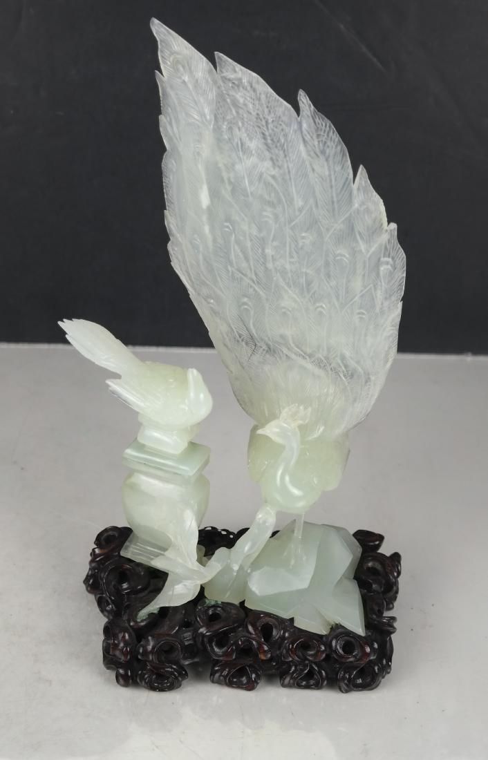 Jade Sculpture of Peacock and Bird: Jade sculpture of a peacock on rocks and a bird perched on an urn, attached to a carved wood base. [11 x 6 x 3 1/2 inches]. In good condition.