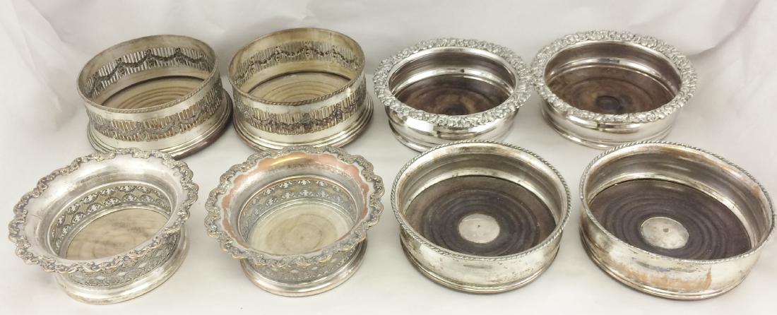4 Pairs English Silver-Plated Wine Bottle Coasters: Lot of 8 items comprising four pairs of antique English silver-plated wine / champagne bottle coasters. Repousse, reticulated, with wood bottoms. [Sizes from 5 1/2 (dia) inches to 6 1/2 (dia) inches].