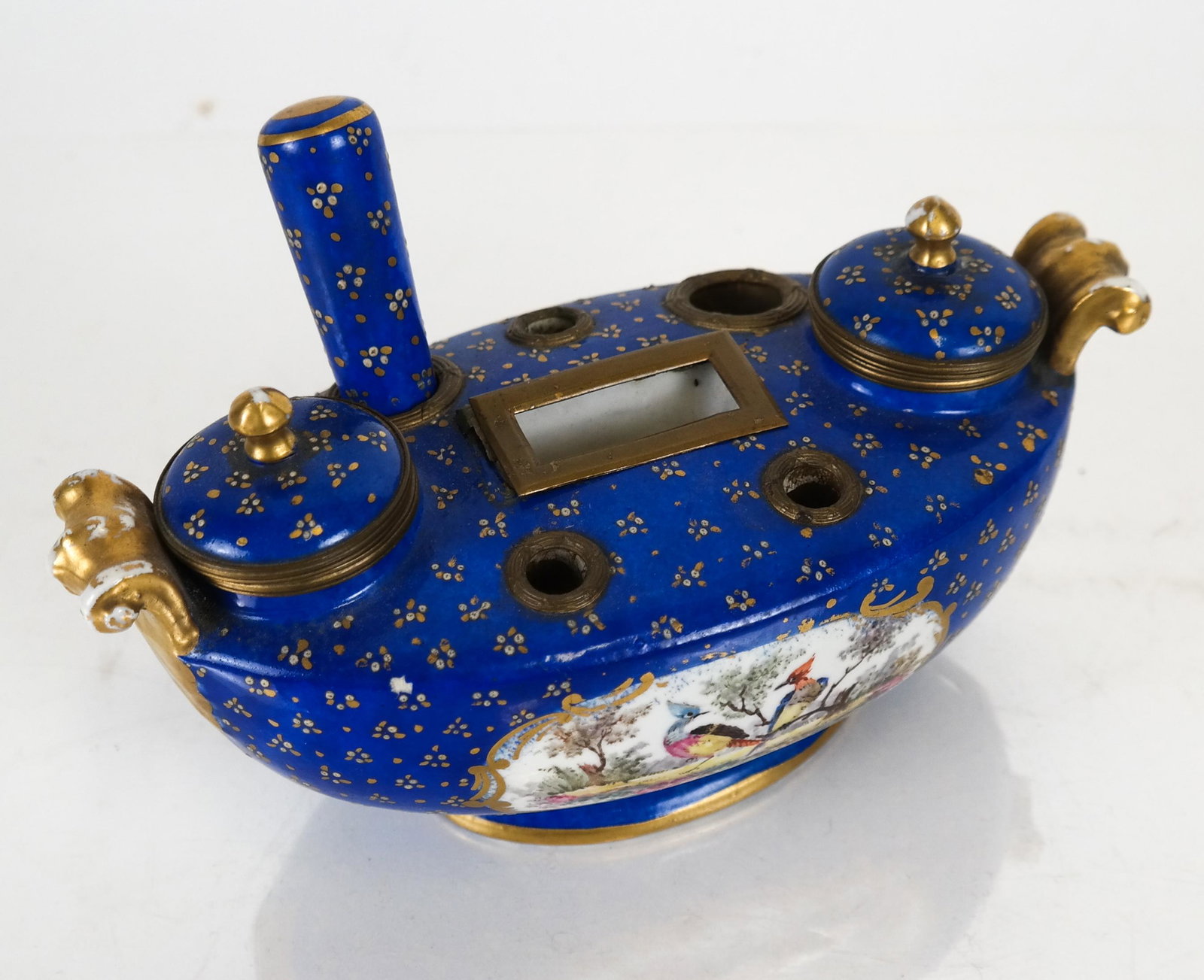 Sevres Gilt Porcelain Inkwell: Sevres inkwell decorated with birds, with hinged well covers and a seal. [4 x 8 x 4 inches]. Center compartment rim has old glue and needs re-attaching; wear to gilt.