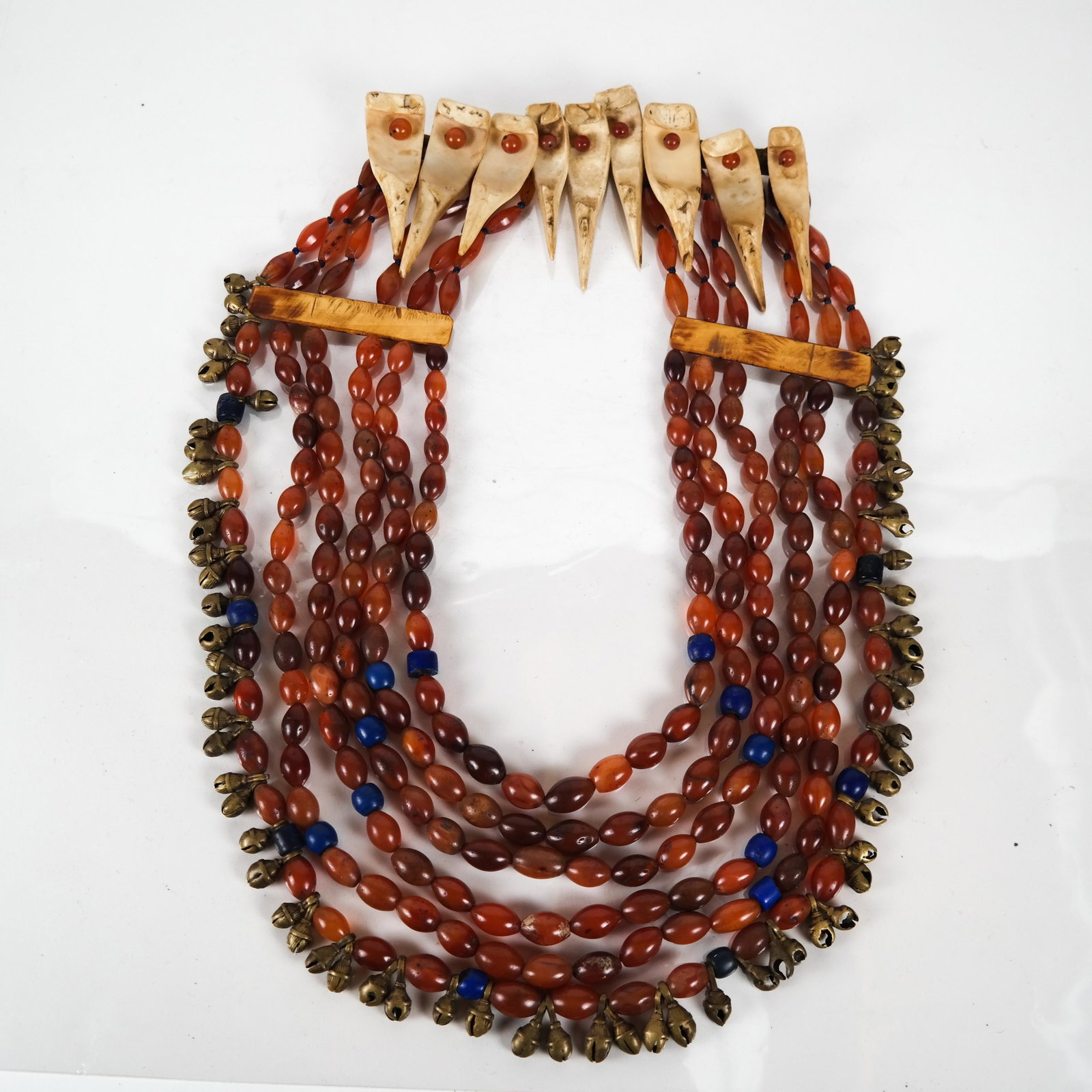 Tribal Bone and Carnelian Necklace: Tribal multi-strand necklace, composed of five strands of orange carnelian oval beads with occasional blue-colored small cylindrical beads, the longest strand also suspending small brass bells, the ba