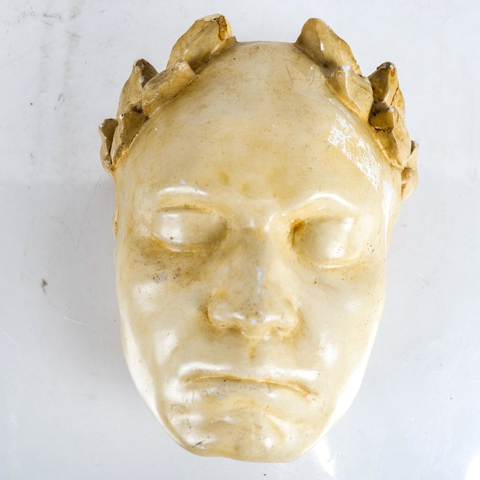 Plaster Roman-Style Death Mask: Roman-style plaster death mask. [8 1/2 x 7 1/2 x 3 1/2 inches]. Chips and repairs to laurel leaves.