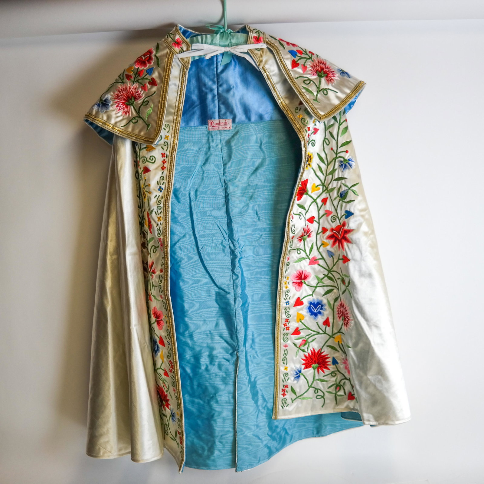 Floral Embroidered Bullfighting Cape from Spain: Rare embroidered satin cape from Spain, typically a ceremonial bullfighting cape, with polychromatic stylized viscose flowers on an off-white bemberg ground, edged with gold metallic cording and sequi