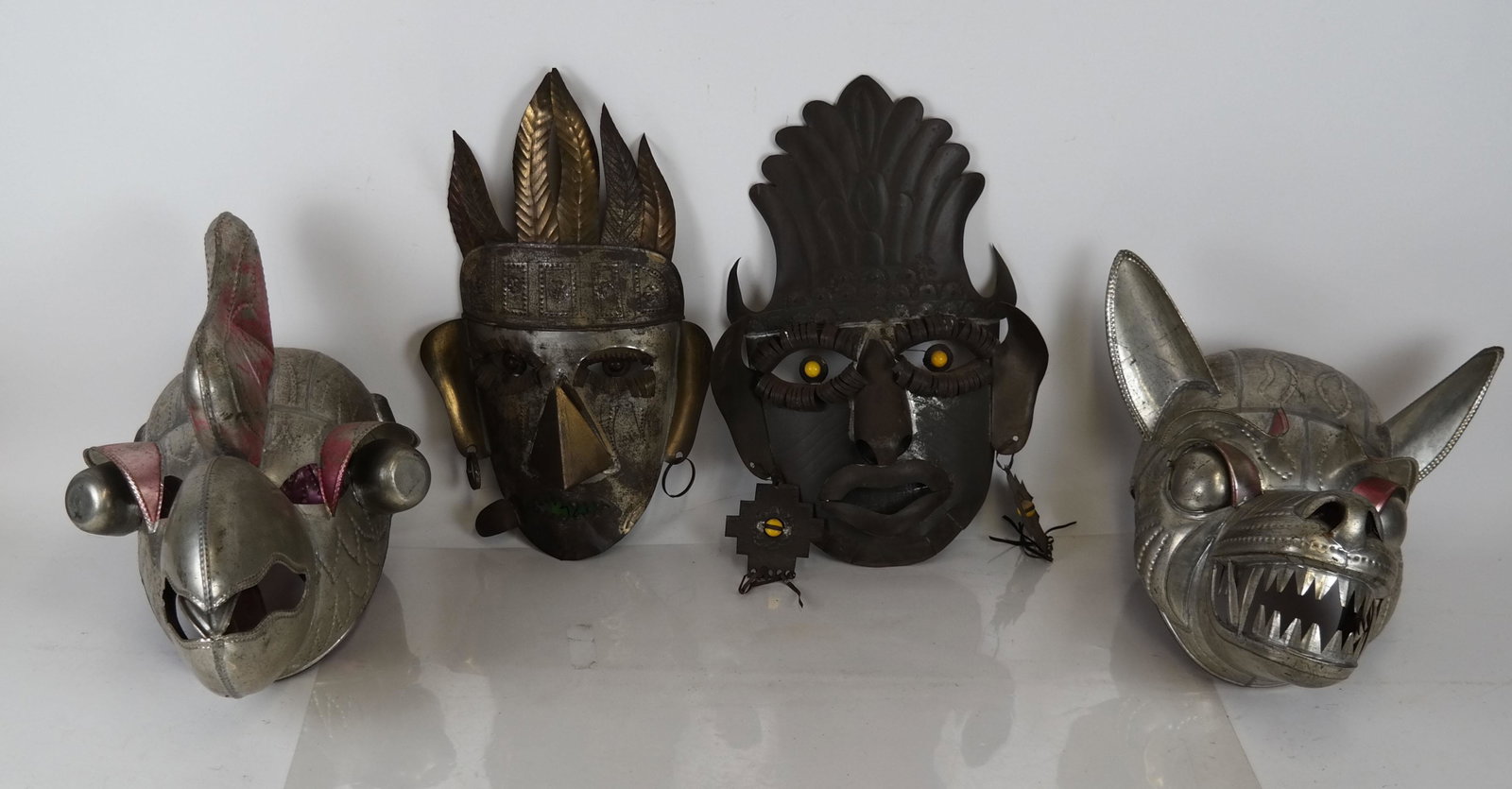 Four Tin Tribal Masks: Two matched bird and wolf forms, together with two others of faces with earrings. [16 x 15 x 12 inches]. All in overall good condition.