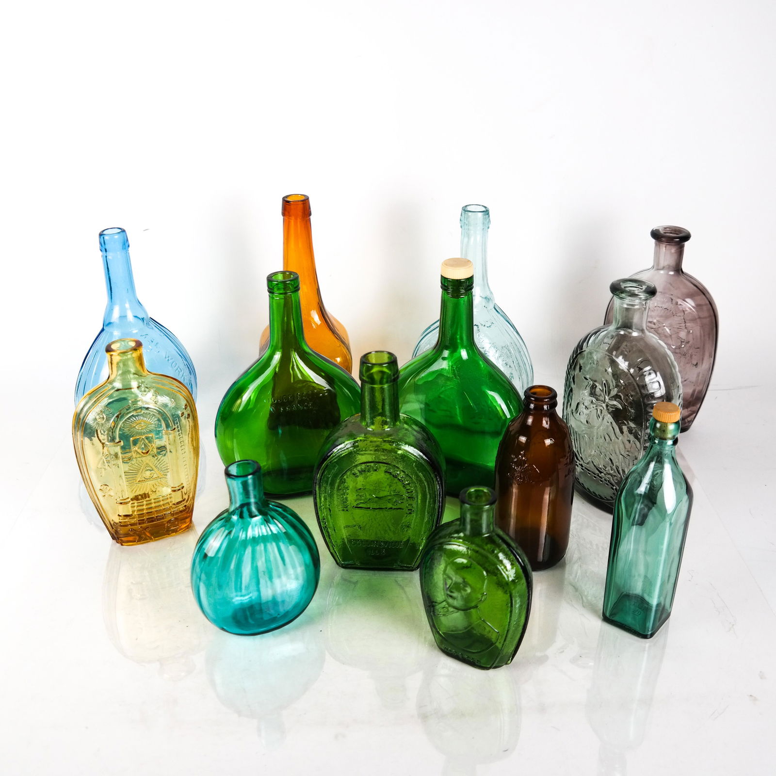 Lot of 13 Glass Bottles & Flasks, 20th C.: Group of blown and molded glass bottles and flasks includes: Empire Glass Works aqua Jenny Lind (x2), two Masonic motif flasks, two "Liquor Bottle / France" flasks, two George Washington molded glass
