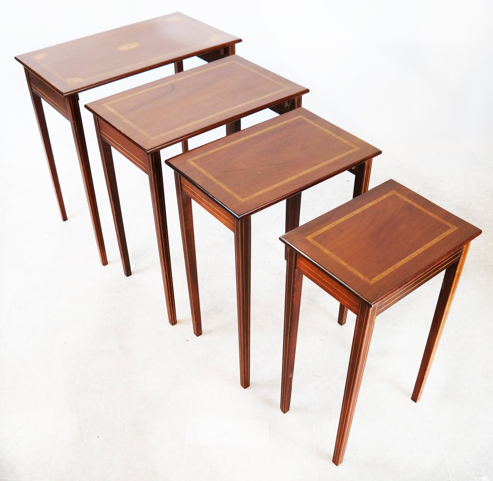 Sheraton-Style Four Nesting Tables: Sheraton-style nest of four tables, mahogany, all inlaid; medallion inlay to top one only. [24" H x 22 3/4" W x 13 3/4" D]. All with cracked veneer.