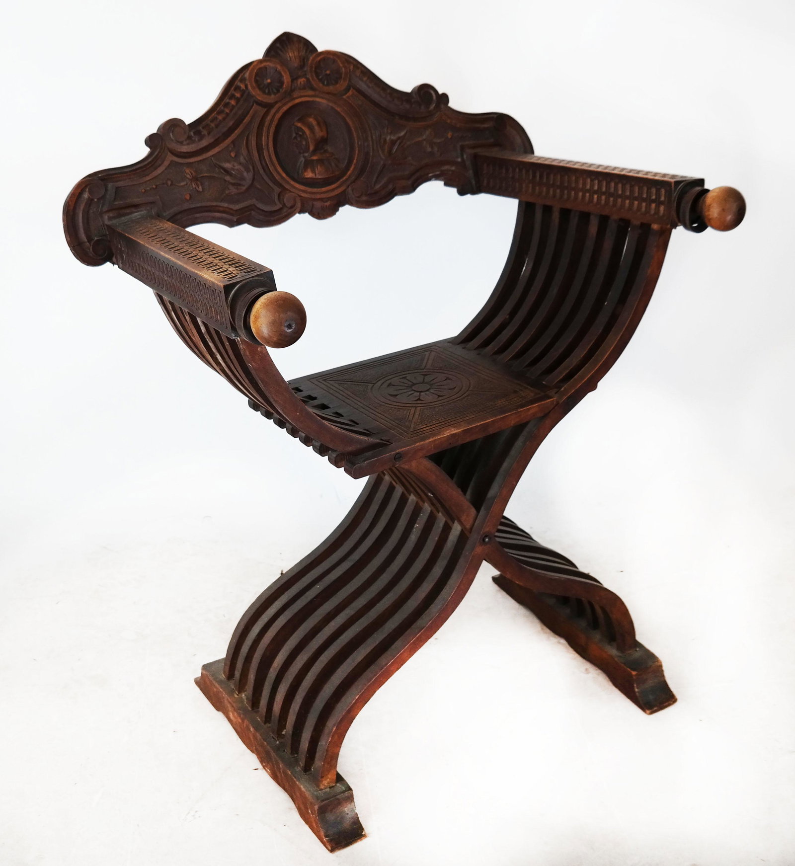 Carved Savonarola Chair: Carved Savanarola chair, with portrait motif and rosette decor. [36" H x 29" W x 22" D; 19 1/2" to seat].